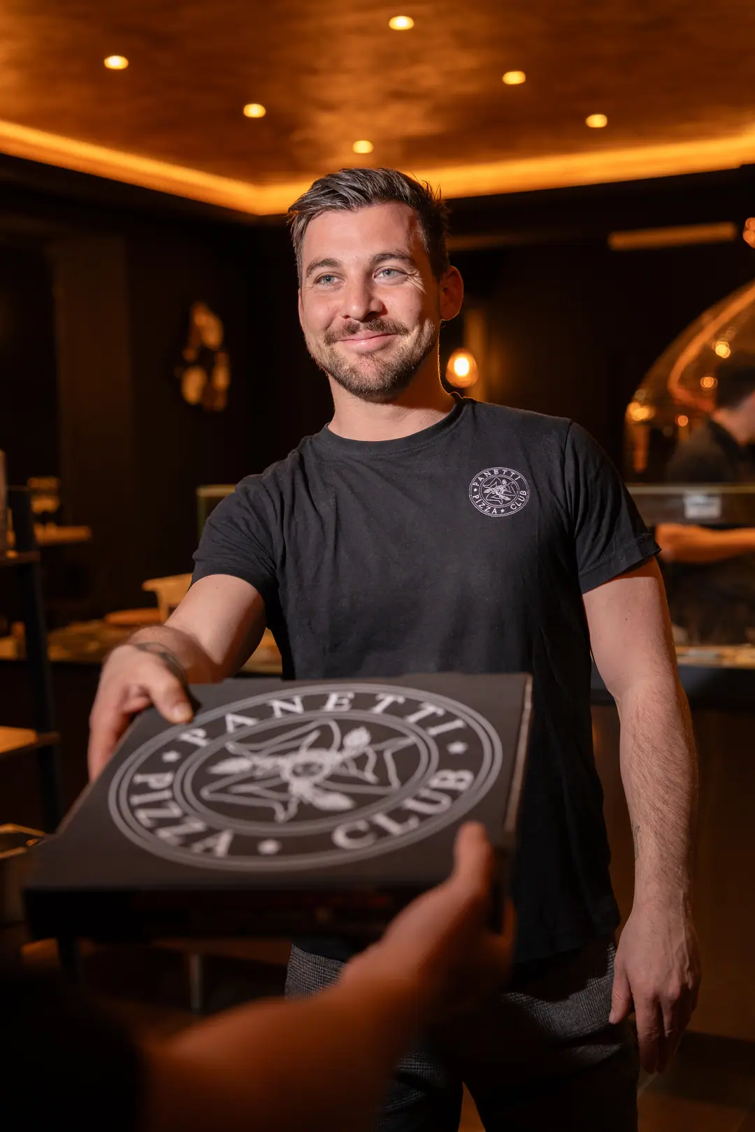 Il pizzaiolo, sorridente, porge un cartone Panetti Pizza Club